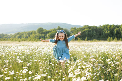 Happy cheerful child girl 3-4 year old wear stylish rustic dress running in meadow with flowers 