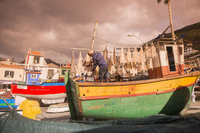 Fishing boats moored at harbor against sky