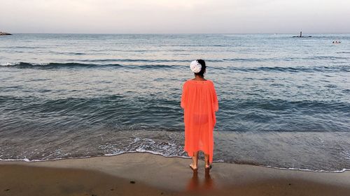 Rear view of woman standing on beach against sky