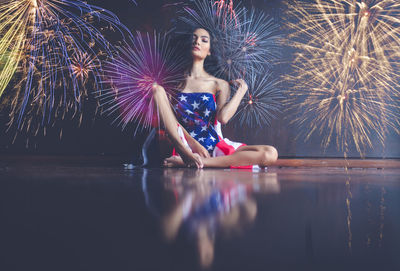 Woman with american flag sitting against firework display