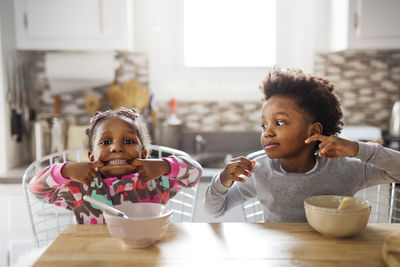 Portrait of playful girl making face while brother looking at her in kitchen