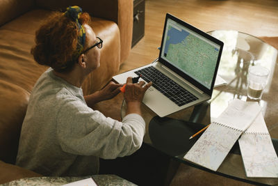 Side view of elderly woman planning trip on map in laptop at home