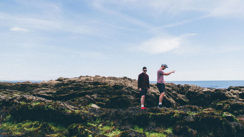 Side view of men walking on rocks against cloudy sky at looe during sunny day