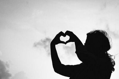 Rear view of silhouette woman holding heart shape against sky