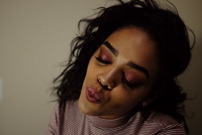 Close-up of woman with eyeshadow and lipstick puckering against wall