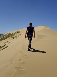 Full length of man walking on sand at desert against clear sky