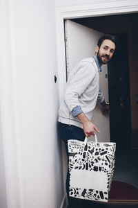 Mid adult man holding shopping bag by open door