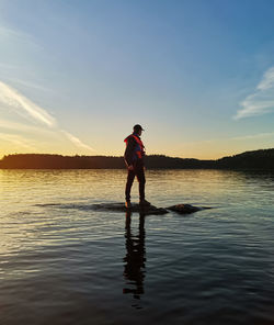 Full length of man standing in lake against sky during sunset