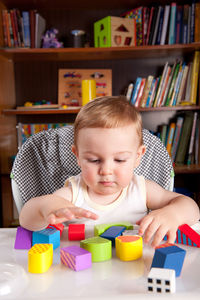 Cute baby boy playing with toy blocks on table