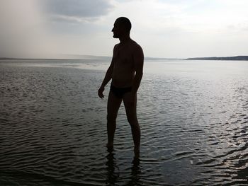 Shirtless man standing in sea against sky
