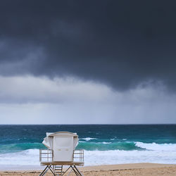 Lifeguard hut on shore at beach against storm clouds