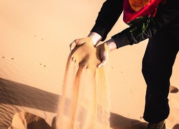 Midsection of person pouring sand at desert 