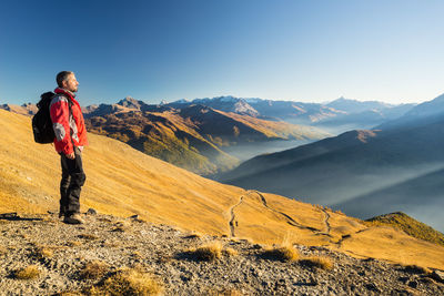 Full length of male hiker standing on mountain against sky during sunny day