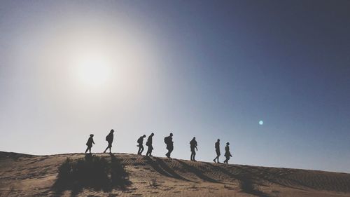Silhouette people walking in desert against clear sky