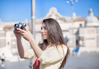 Beautiful woman photographing by historic building against sky