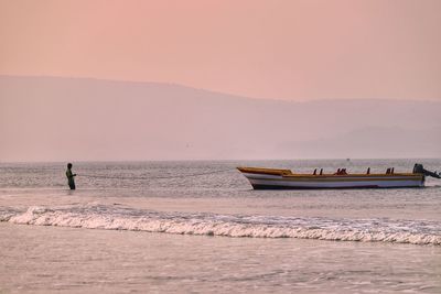 Man pulling boat in sea against sky during sunset