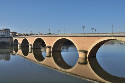 Arch bridge over river against clear blue sky