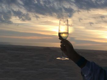 Close-up of hand holding sand at beach against sky during sunset