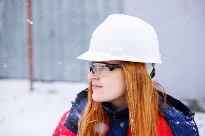 Portrait of woman worker in overalls wearing hat against snow