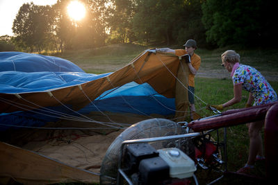 Couple adjusting tent on field against trees