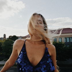 Woman with messy hair standing in city against sky