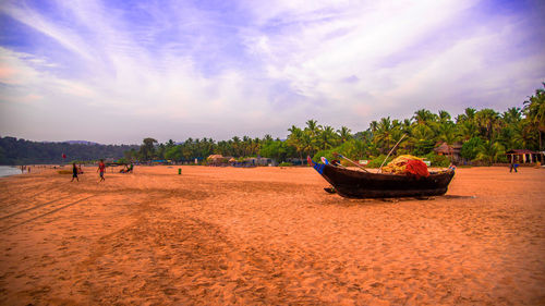 Boats moored on sandy beach against cloudy sky