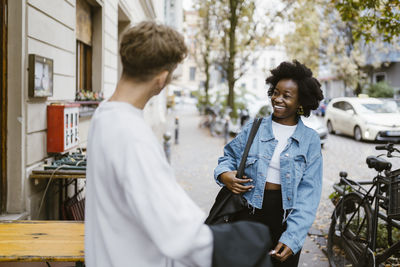 Happy woman walking while meeting boyfriend standing on sidewalk in city