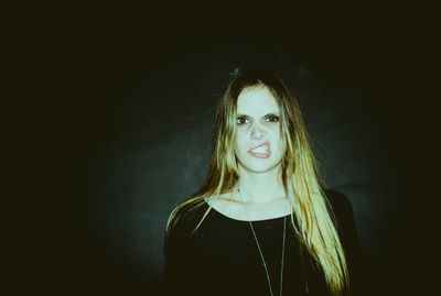 Portrait of young woman making face against black background