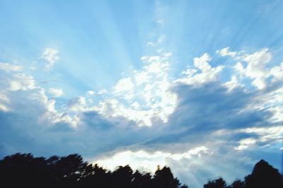 Low angle view of sunlight streaming through clouds