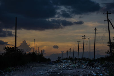 Garbage and electricity pylons on land against cloudy sky during sunset