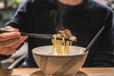 Midsection of man eating food with chopsticks