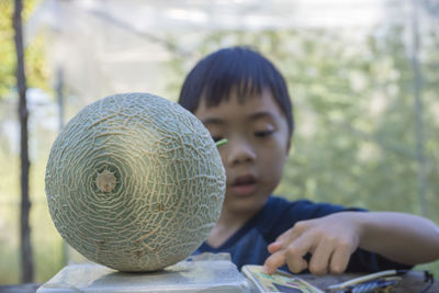 Close-up of boy weighing muskmelon on machine outdoors