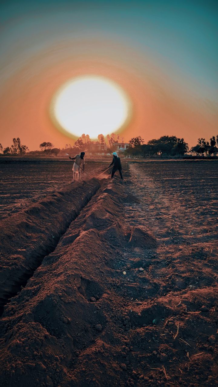 PEOPLE WALKING ON SHORE AGAINST SKY DURING SUNSET