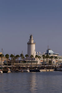 Ship moored at harbor and lighthouse against clear sky