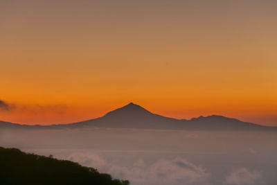 Scenic view of silhouette mountains against orange sky