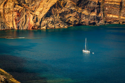 Sailboat sailing on sea against rock formation