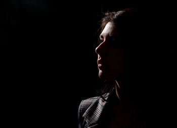 Close-up of woman looking away against black background