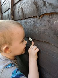 Close-up of boy looking through hole in wooden wall