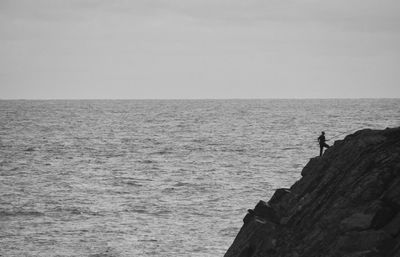 Scenic view of angler on rock against sky