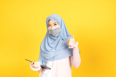 Full length portrait of woman standing against yellow background