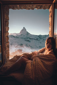 Full length of woman relaxing by window against mountain