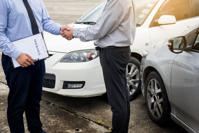 Midsection of car salesperson shaking hands with customer