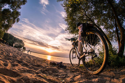Bicycle on beach against sky during sunset