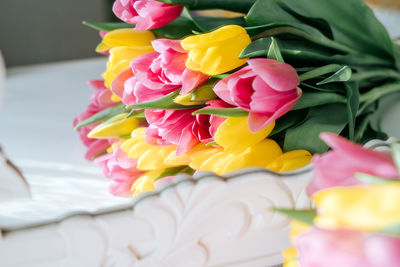 Close up fresh spring yellow and pink tulips bouquet on white wood table background in mirror
