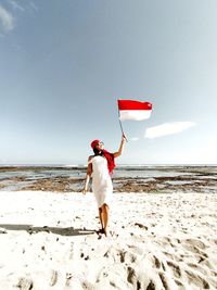 Rear view of woman walking on beach holding flag