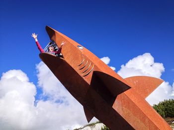 Low angle view of woman in shark statue against blue sky