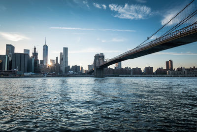 Low angle view of brooklyn bridge over east river by cityscape against sky