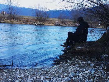 Man sitting by lake against sky