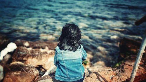 Rear view of girl sitting at beach on sunny day