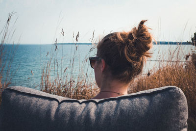 Rear view of woman sitting on couch against lake